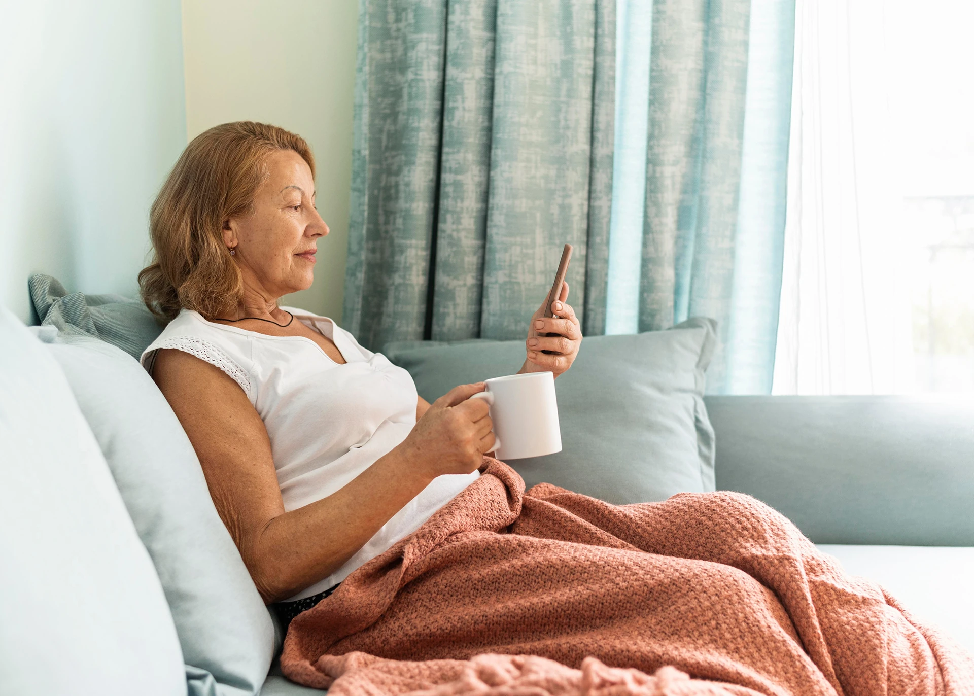 Patiente à domicile consultant son smartphone, installée dans son canapé